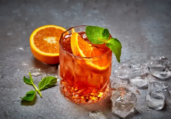 Rinfrescante cocktail con ghiaccio tritato, arancia e menta. Perfetto per un aperitivo estivo.