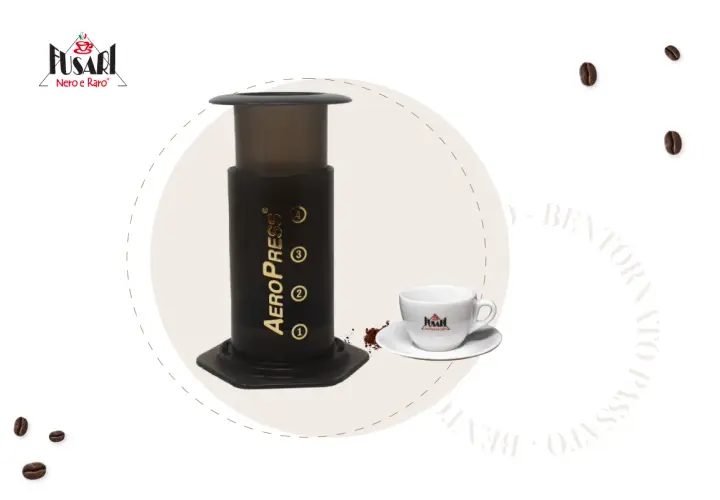 AeroPress per un caffè perfetto. Accanto, una tazzina bianca con logo e chicchi di caffè sparsi.