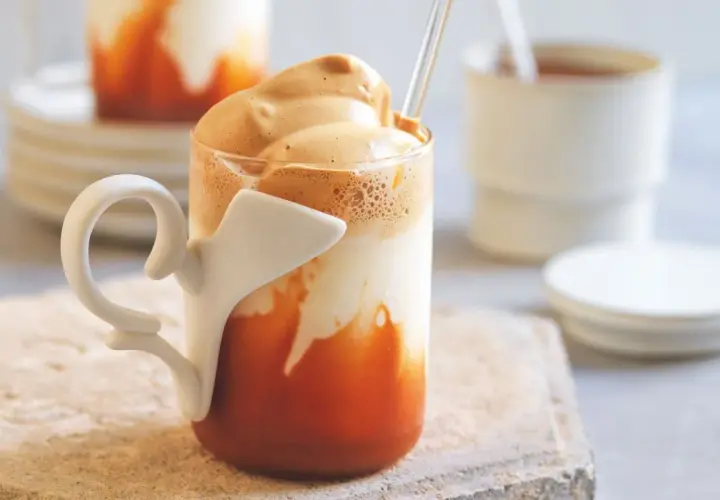 Un bicchiere di caffè freddo con schiuma cremosa e latte di mandorla, servito con una cannuccia.