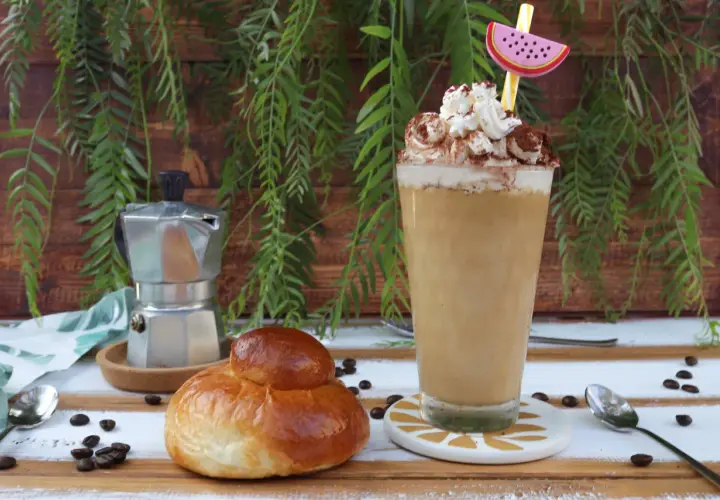 Un bicchiere di caffè freddo siciliano con panna e cacao, accanto a una brioche e una moka.