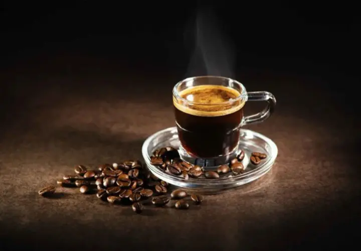 Un fumante caffè al vetro, con chicchi tostati sparsi attorno, evoca un momento di puro piacere.