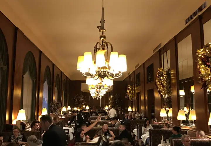 Interno elegante di uno dei caffè storici di Vienna, con tavoli apparecchiati, clienti e lampadari imponenti.