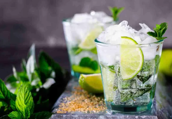 Due bicchieri di mojito, con menta fresca, lime e ghiaccio tritato. La ricetta perfetta per un'estate rinfrescante.