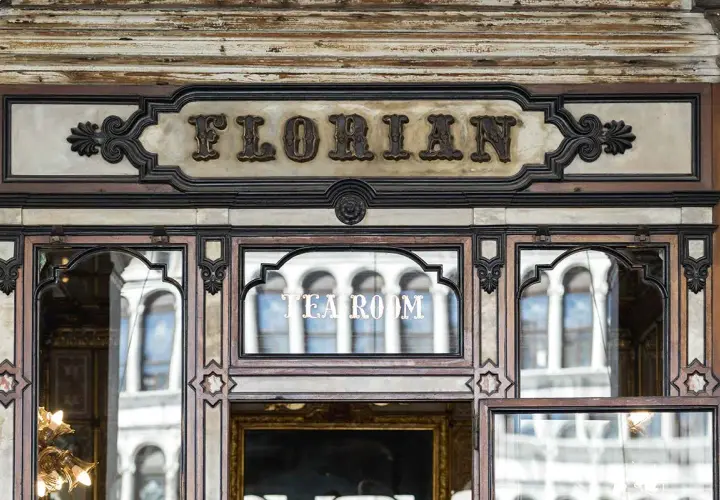 Ingresso del storico **Cafe Florian**, con insegna in rilievo e riflessi di palazzi veneziani nelle vetrate.
