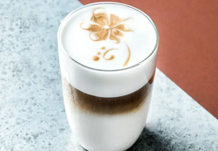 Un delizioso cappuccino freddo con schiuma decorata a forma di fiore, servito in un bicchiere trasparente.