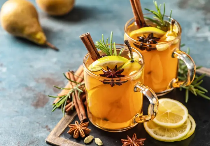 Due bicchieri di grog bevanda calda, guarniti con cannella, anice stellato, limone e rosmarino.