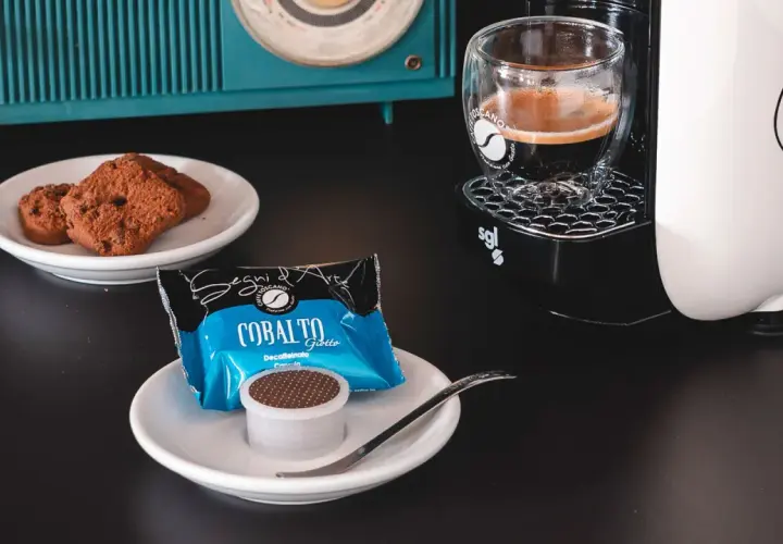 Un caffè decaffeinato pronto per essere gustato, accompagnato da biscotti al cioccolato e una macchina da caffè moderna.