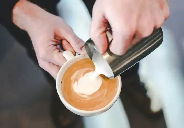 Mani esperte versano latte per cappuccino, creando un disegno sulla schiuma.