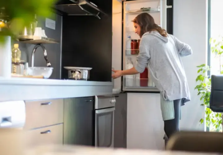 Donna prende una bottiglia dal frigo. Forse cerca il caffè in frigo per preparare una bevanda rinfrescante.