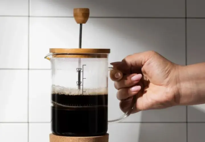 Mano che tiene una french press con caffè scuro. La scelta del quale caffè per french press è fondamentale per un aroma intenso.