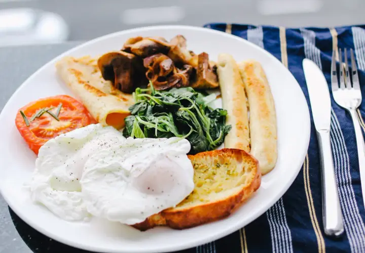 Un piatto ricco per una colazione continentale: uova in camicia, pomodoro, funghi, spinaci, pane tostato e salsicce.