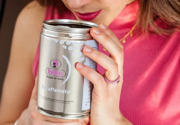 Donna annusa una lattina di caffè decaffeinato, godendosi l'aroma. Un caffè con meno caffeina, perfetto per ogni momento.