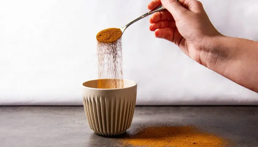 Mano versa polvere da un cucchiaio in una tazza. Forse è caffè solubile, ma fa male.