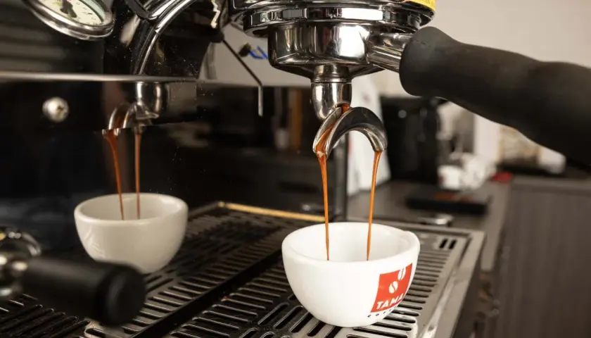 Due tazze bianche ricevono il prezioso liquido scuro, il caffè espresso, dalla macchina professionale.