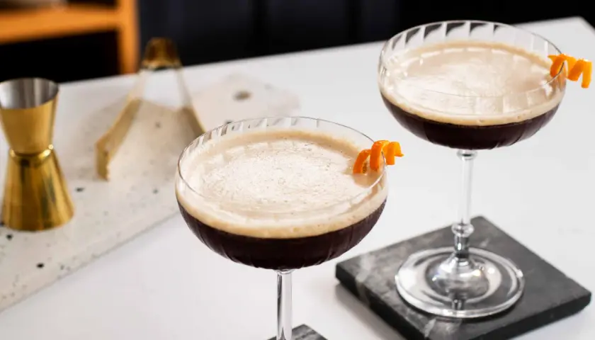 Due cocktail scuri con schiuma chiara, guarniti con scorza d'arancia. Un'idea per un caffè e succo d'arancia rivisitato.