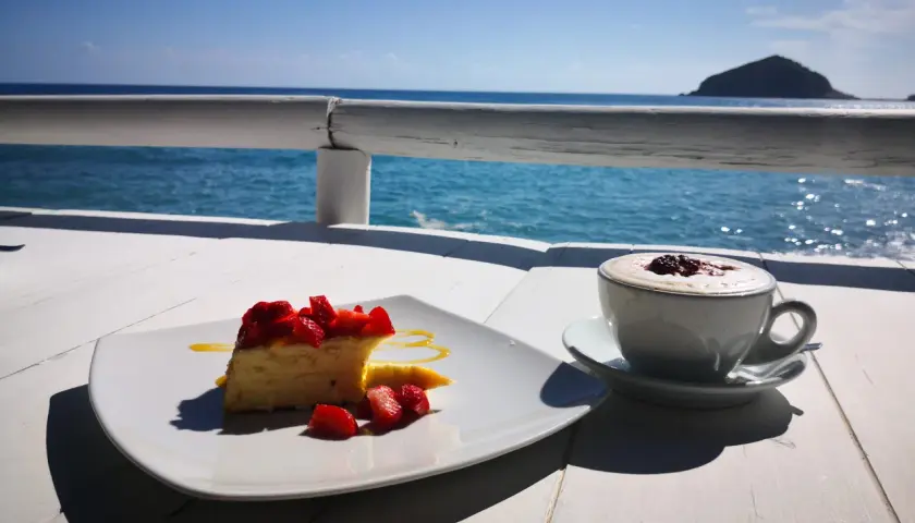 Un dolce con fragole e un caffè fumante, con il mare azzurro e un'isola all'orizzonte. Un momento di puro relax con un caffè al mare.