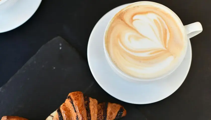 Un cappuccino con latte art a forma di cuore e croissant per una perfetta colazione al bar.