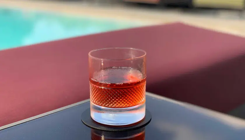 Un bicchiere di Sazerac, cocktail IBA, riposa su un tavolino vicino a una piscina.
