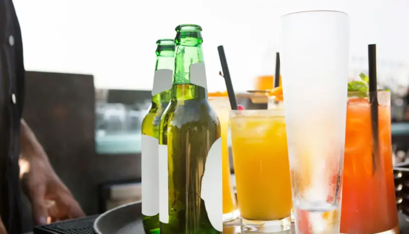 Un cameriere serve un aperitivo originale: birre fresche e cocktail colorati su un vassoio.