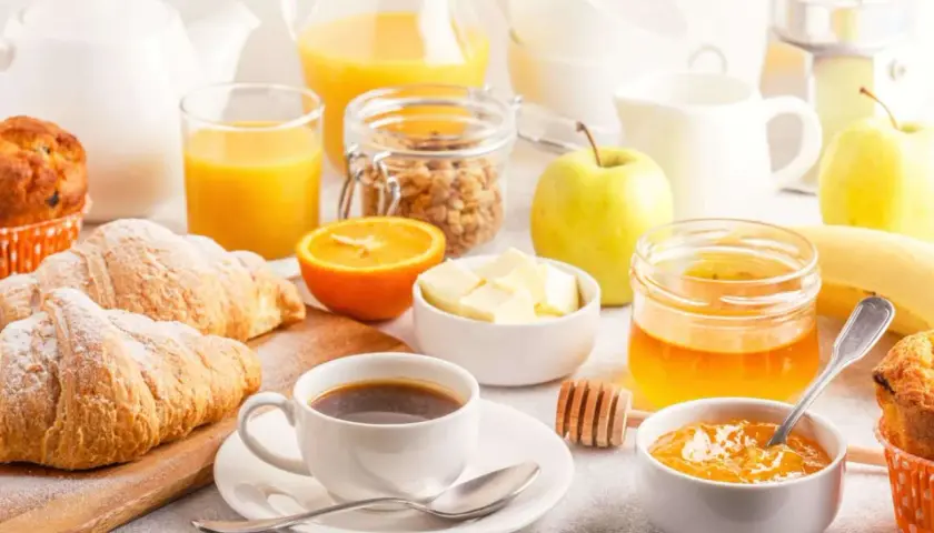 Un tavolo imbandito con croissant, caffè, succo d'arancia, frutta e marmellata, perfetto per delle bevande per colazione.