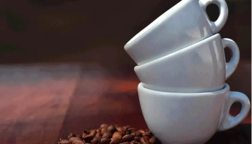 Tre tazzine bianche impilate, con chicchi di caffè tostati in primo piano. Immagina quanto contiene una tazzina di caffè.
