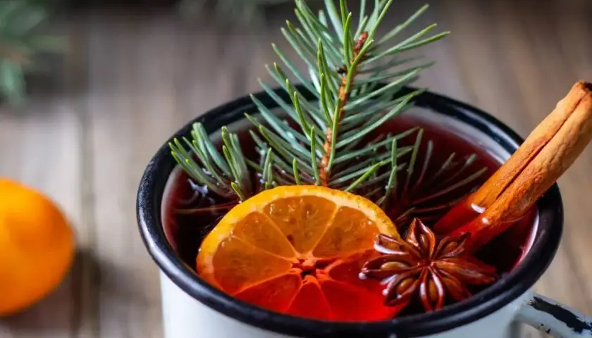 Un bicchiere di punch caldo, con arancia, cannella e anice stellato, decorato con un rametto di pino. Perfetto per le serate invernali.