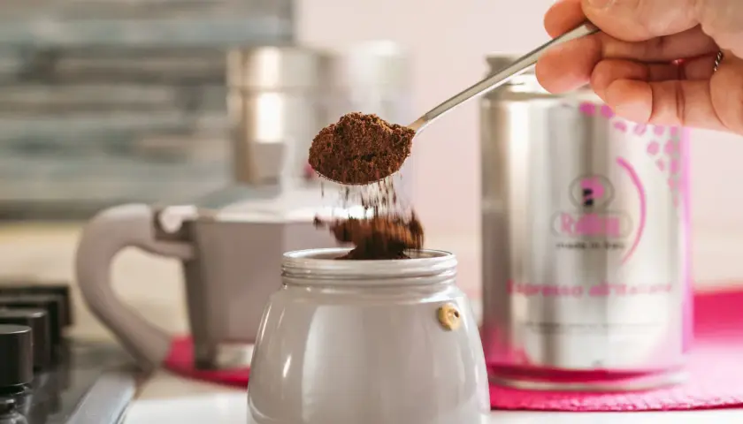 Un cucchiaino di caffè macinato cade nel bricco di una caffettiera, un ricordo di come si faceva il caffè prima della moka.
