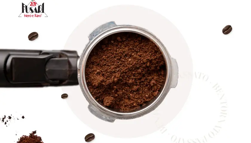 Macinatura caffè fine nel portafiltro, pronta per un espresso perfetto. Chicchi sparsi e logo Fusari.