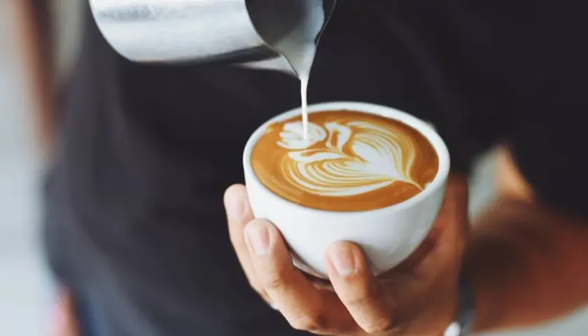 Un barista crea un disegno a latte art su un cappuccino, un'opera d'arte cremosa.