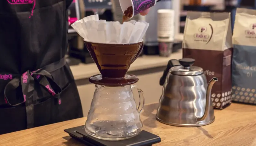 Preparazione di un caffè drip. Caffè macinato versato in un filtro, bollitore e sacchetti di caffè sullo sfondo.