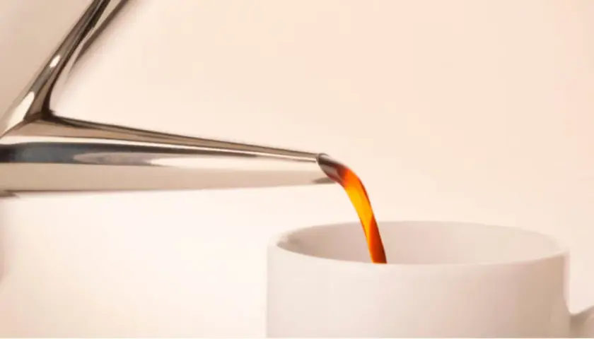 Caffè caldo versato da una cuccuma napoletana in una tazza bianca.