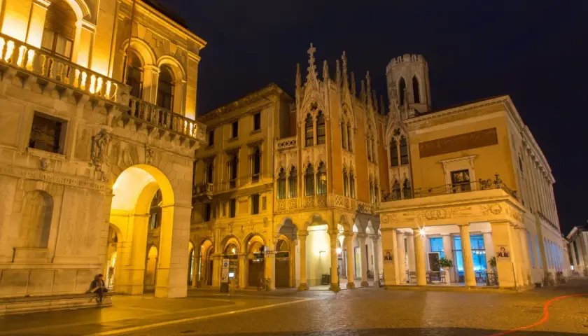 Edificio storico illuminato di notte a Padova, con archi e dettagli gotici. Un luogo che evoca il fascino di un **caffè storico Padova**.