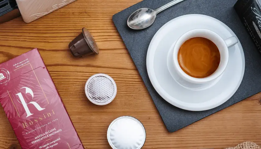 Vari tipi di caffè in capsule, una tazzina di espresso fumante e la confezione Rossini.