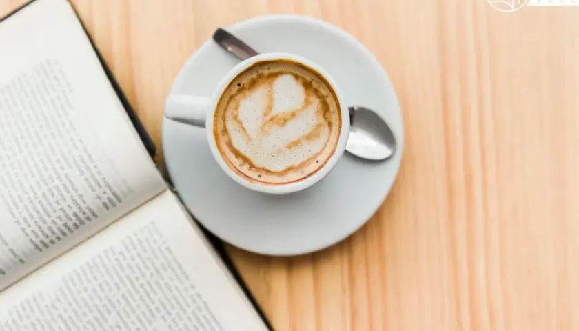 Un libro aperto e una tazza di caffè con schiuma, un invito al caffè illuminismo, su un tavolo di legno.