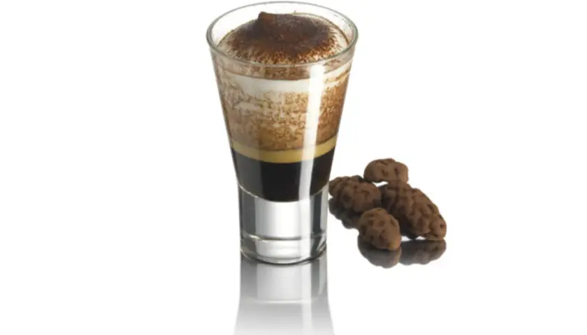 Un bicchierino di caffè con schiuma e cacao, accompagnato da dolcetti al cioccolato.