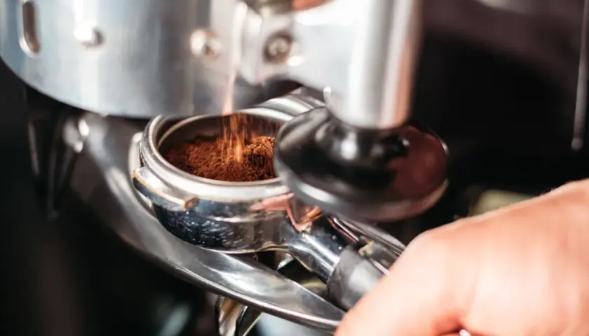 Macinatura caffè bar: polvere scura cade nel portafiltro, pronta per un espresso perfetto.