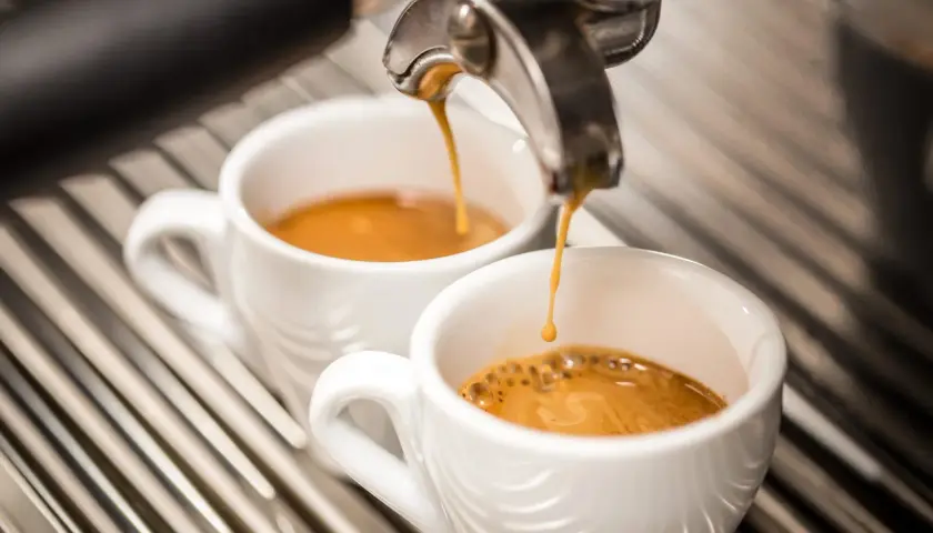 Due tazzine di caffè espresso vengono riempite da una macchina, ma il sapore bruciato del caffè rovina l'esperienza.