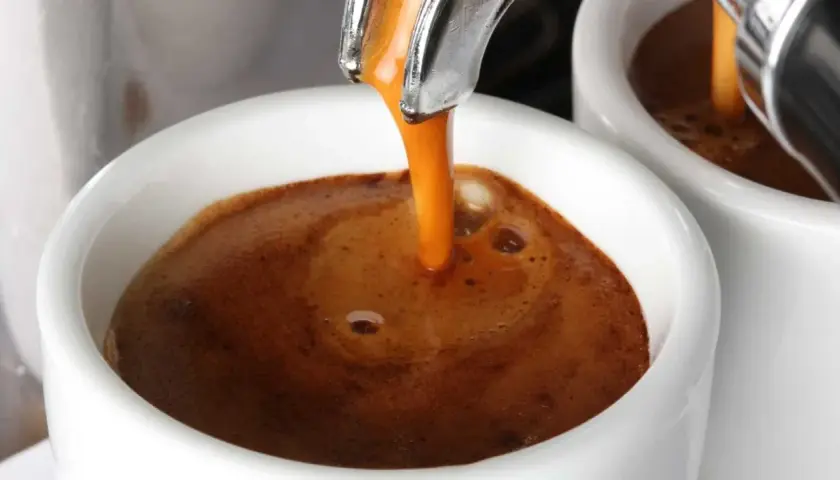 Un filo dorato di caffè caldo si riversa in una tazzina bianca, creando una crema invitante. Un buon caffè per iniziare la giornata.
