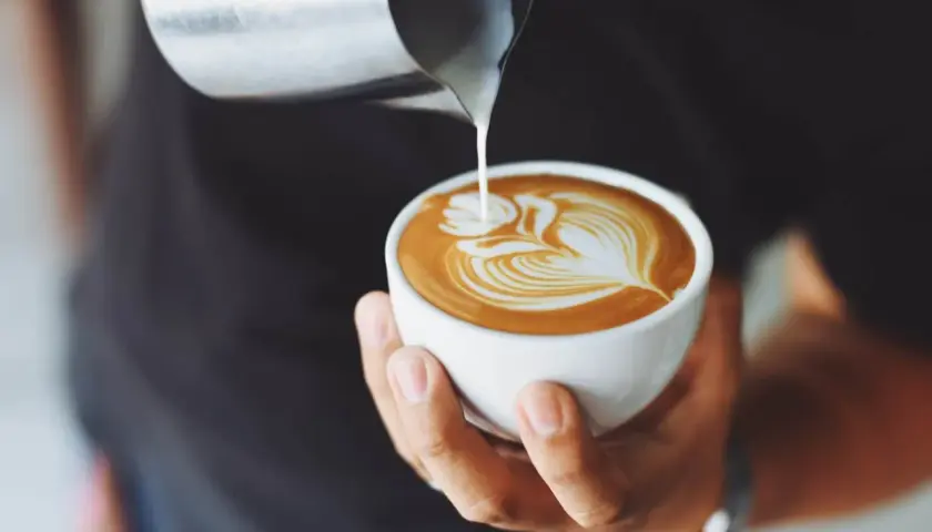 Un barista versa latte montato su un espresso, creando un disegno di latte art. Ecco come si fa il cappuccino perfetto.