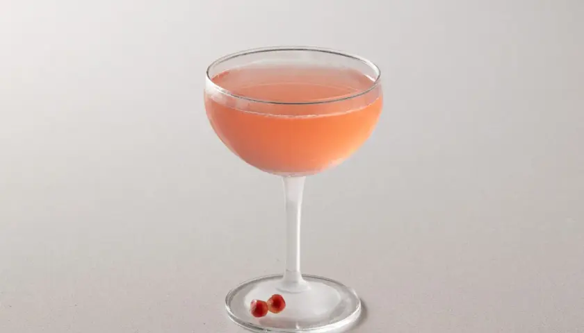 Cocktail rosa in coppa, perfetto per la tua bacardi cocktail ricetta. Due chicchi di melograno sul piattino.