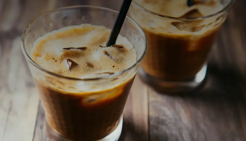 Due bicchieri di **cold brew** con ghiaccio e cannucce nere su un tavolo di legno.