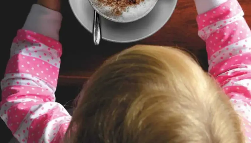 Bambini che gustano un caffè decaffeinato, con una tazza di cappuccino spolverato di cacao.
