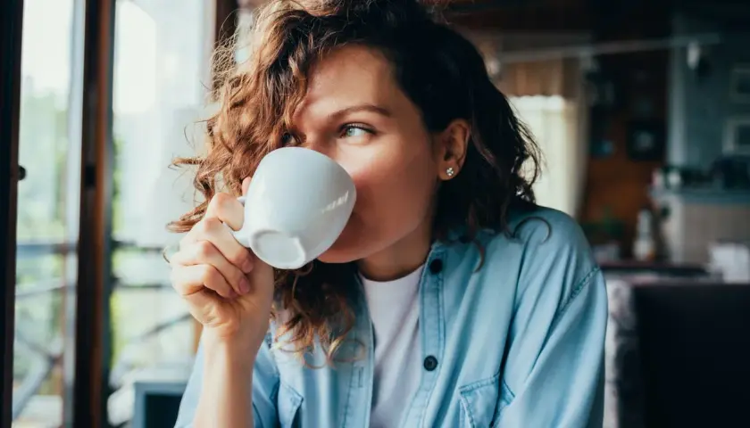 Donna con capelli ricci beve una tazza di caffè, un momento di relax con potassio naturale.
