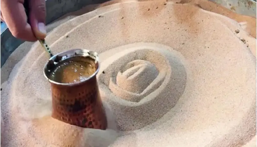Un cezve di caffè turco viene preparato nella sabbia calda, creando un vortice invitante.