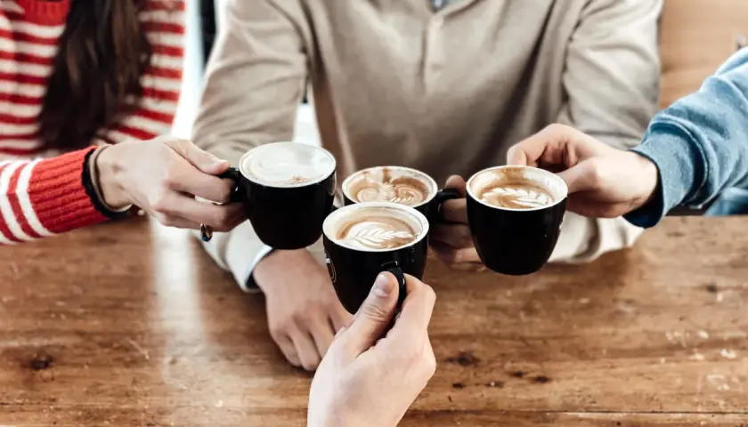 Un brindisi con caffè al bar con amici. Quattro tazze nere con schiuma artistica si avvicinano su un tavolo di legno.