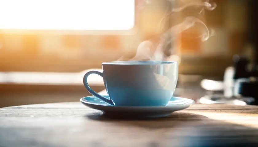 Tazza azzurra fumante su un tavolo di legno. Nonostante il suo aspetto invitante, il caffè è cancerogeno.