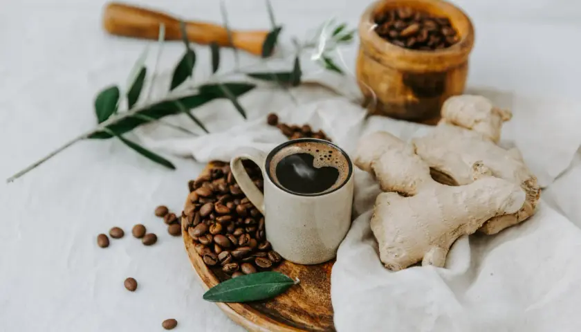 Tazza di caffè messicano fumante, chicchi tostati, zenzero fresco e un rametto d'ulivo su un panno di lino.