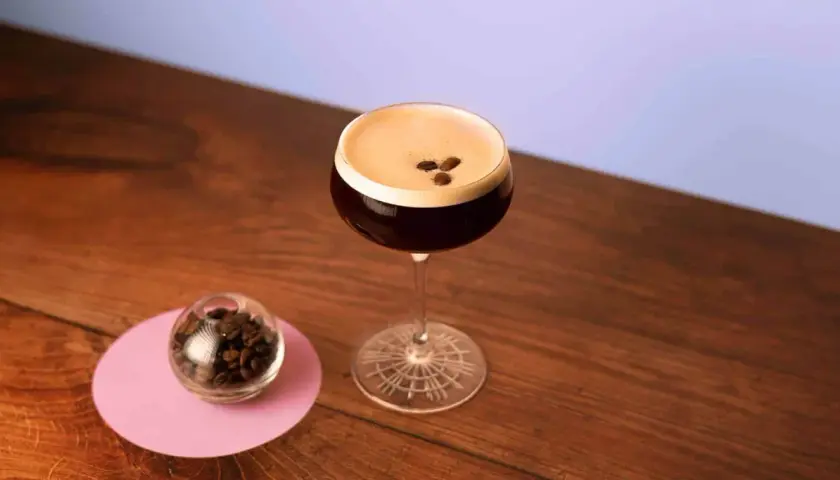 Un elegante cocktail espresso martini, con chicchi di caffè a guarnire, accanto a una piccola sfera di vetro piena di chicchi.