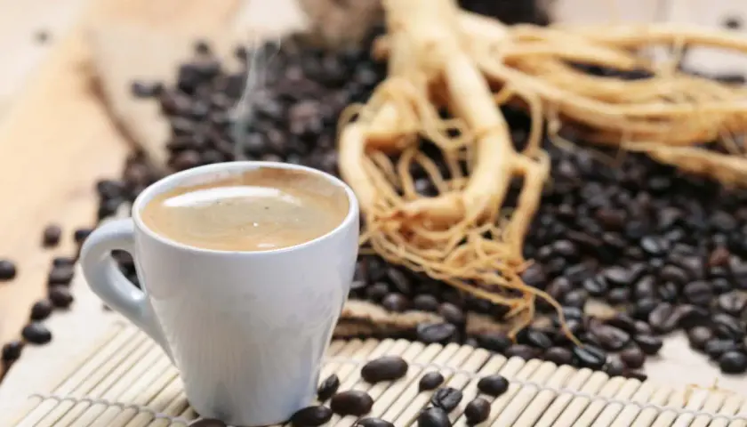 Tazza di caffè fumante accanto a chicchi tostati e radice di ginseng, che contiene caffeina per un risveglio energico.