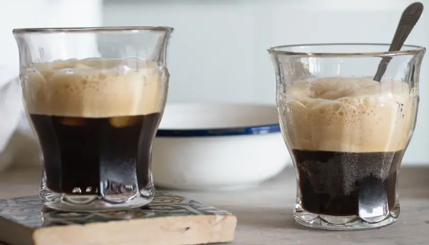 Due bicchieri di caffè shakerato cremoso, con la schiuma dorata che sovrasta il caffè scuro. Uno ha un cucchiaino.
